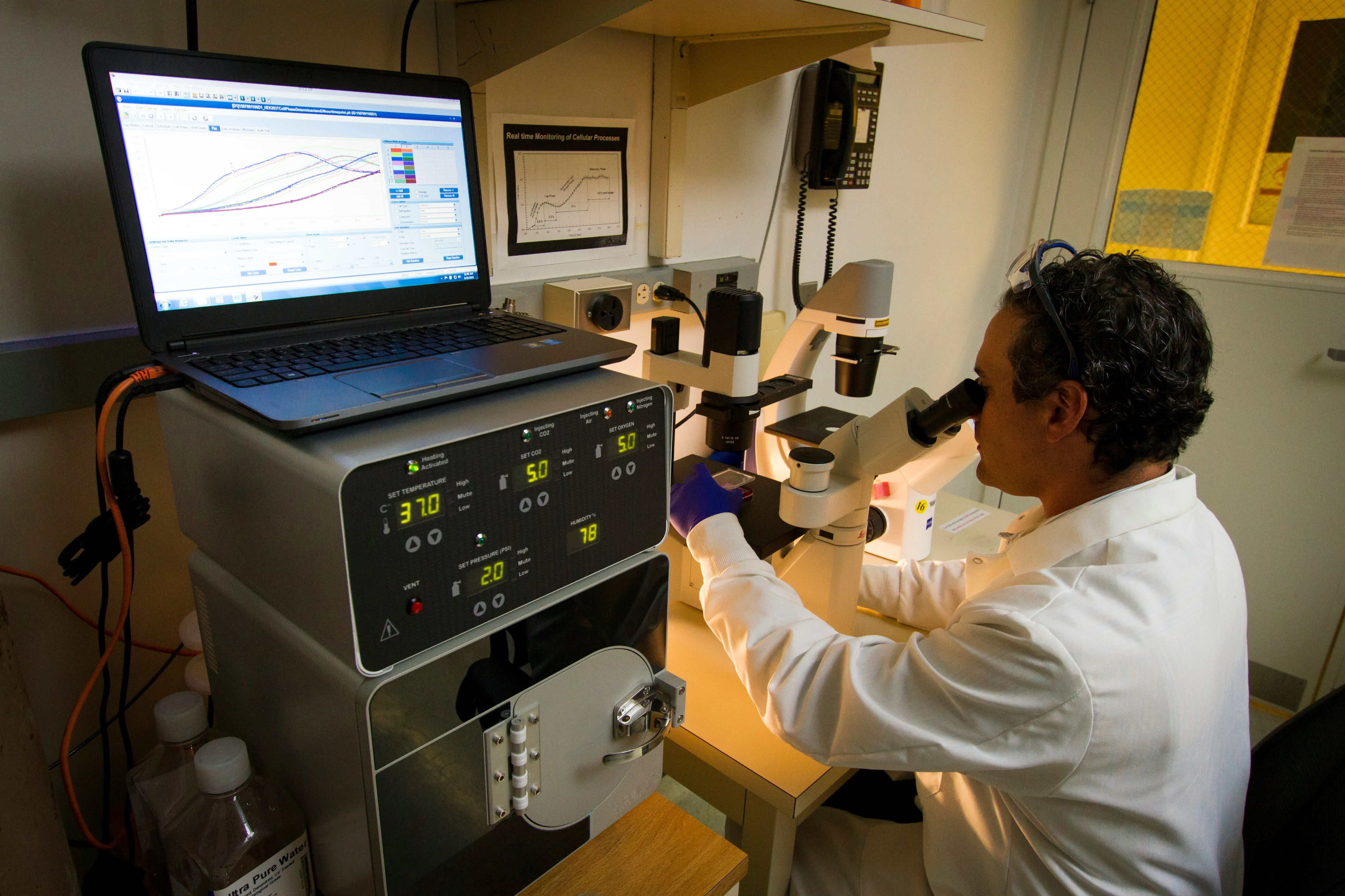 Seth Brodie at a microscope beside a live-cell imaging system, National Cancer Institute